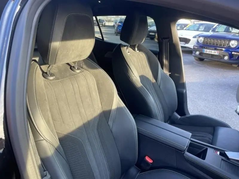 Vue intérieure des sièges avant en cuir noir de la Peugeot 408 Hybrid 136 cv GT e-DCS6, avec accoudoir central et ouverture de porte côté gauche.