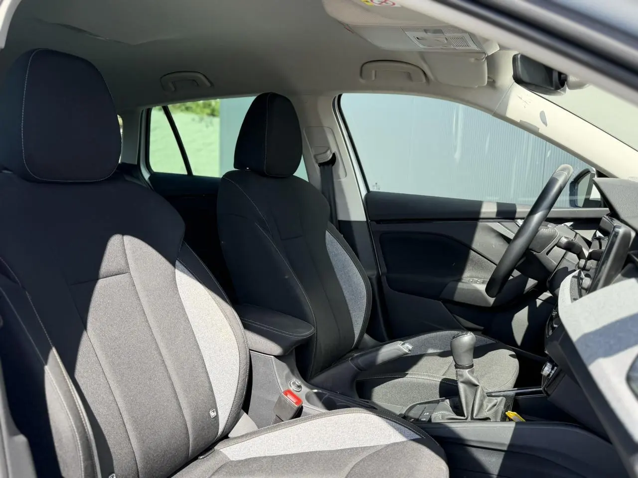 Intérieur de la Skoda Scala TSI 116 blanc Glacier vu côté droit, sièges tissu noir et gris avec accoudoir central.