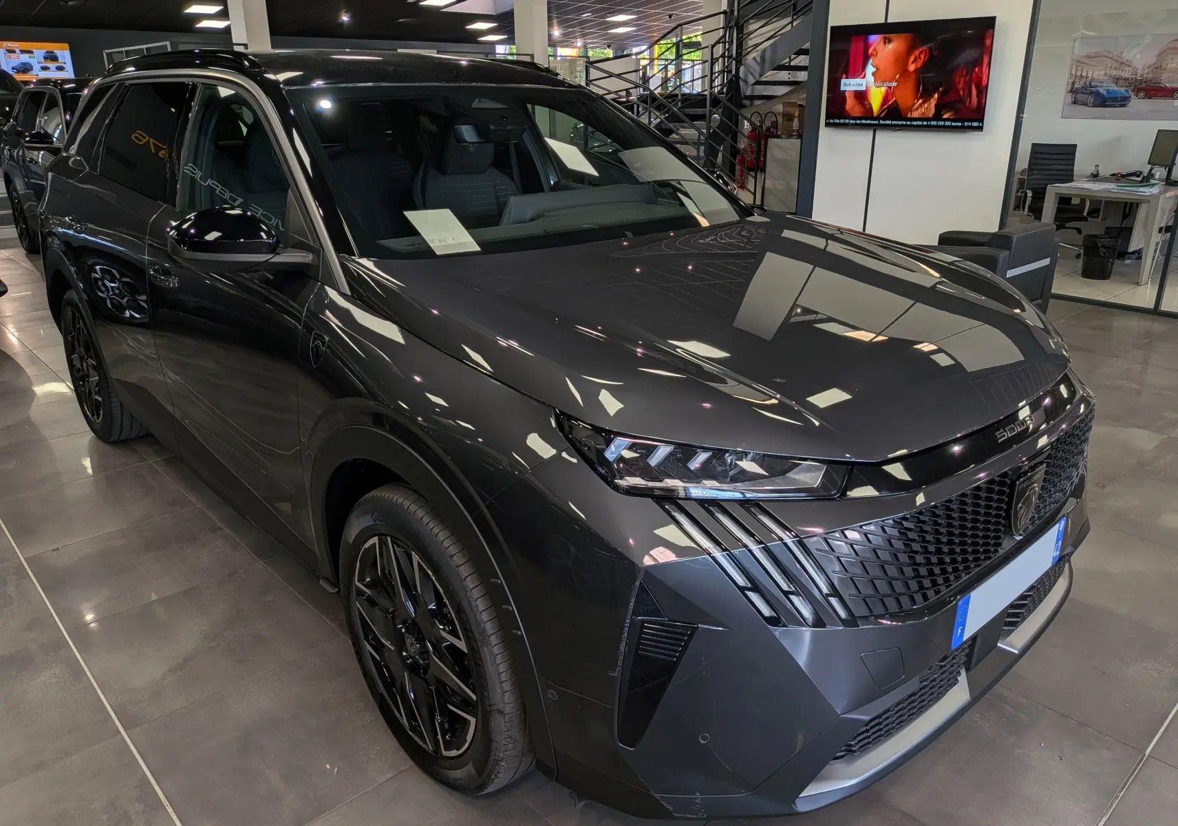 Vue 3/4 avant droit du Peugeot 5008 Hybrid gris titane avec toit noir et calandre au design moderne en concession.