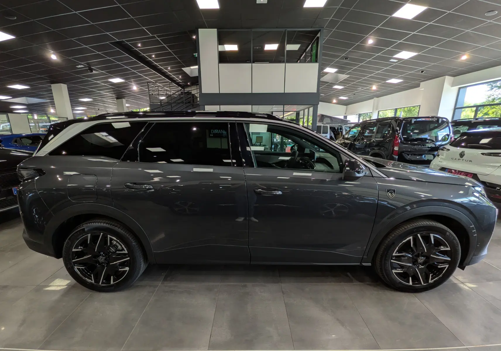 Vue de profil côté droit du Peugeot 5008 Hybrid gris titane avec toit noir et jantes noires en concession.