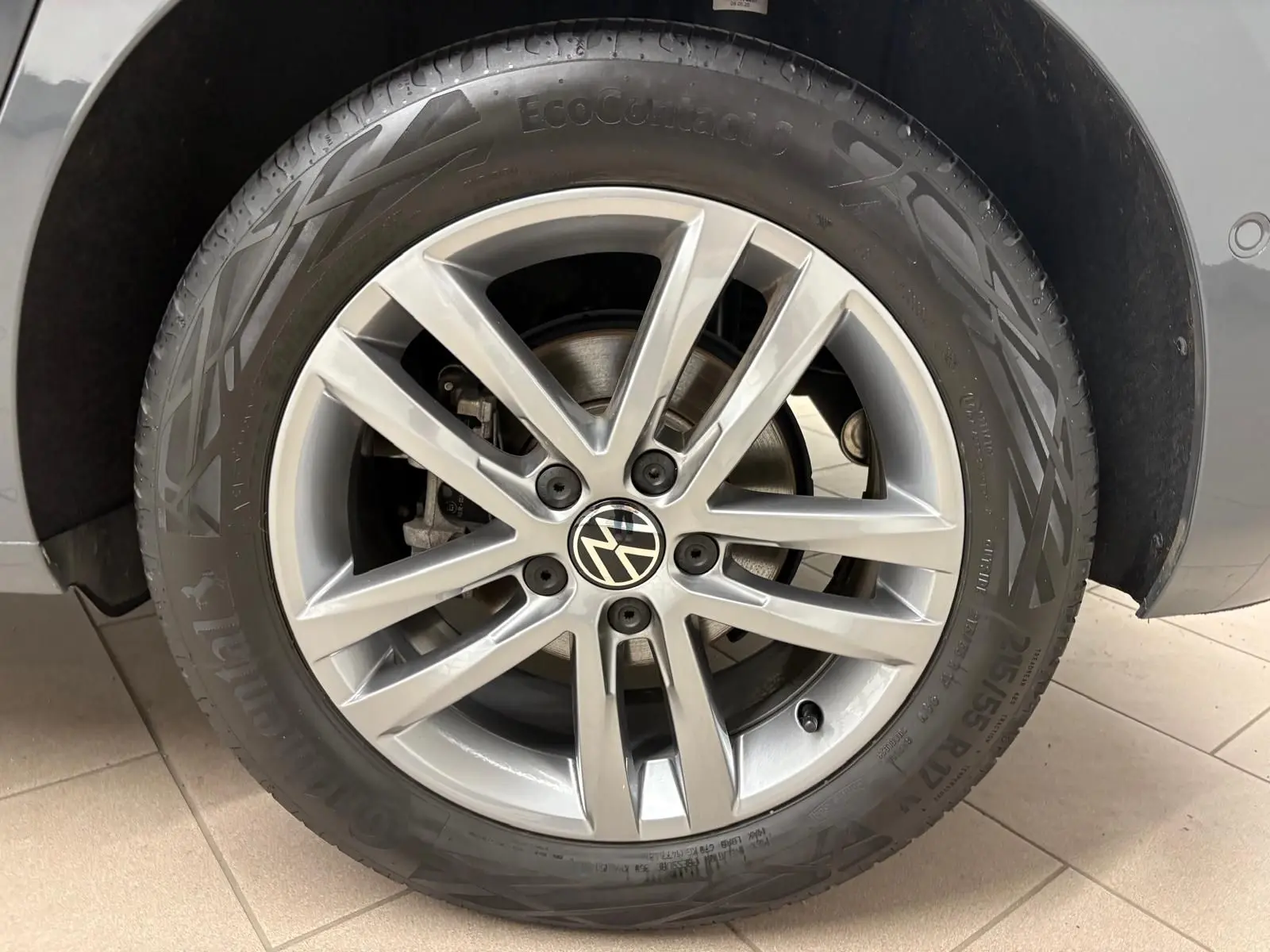 Gros plan sur la roue avant droite en alliage du Volkswagen Touran gris Dauphin, mettant en valeur le logo VW central.