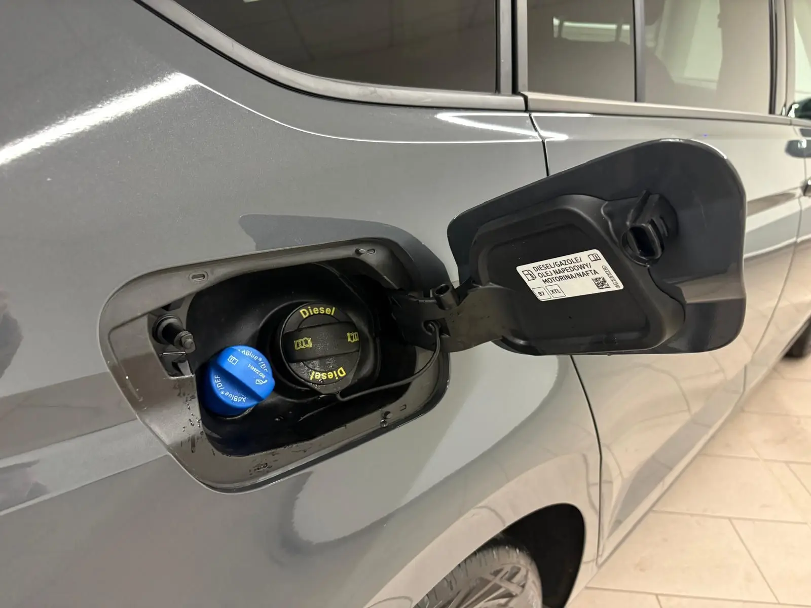 Gros plan sur la trappe à carburant côté gauche d’un Volkswagen Touran gris Dauphin avec bouchons Diesel et AdBlue visibles.