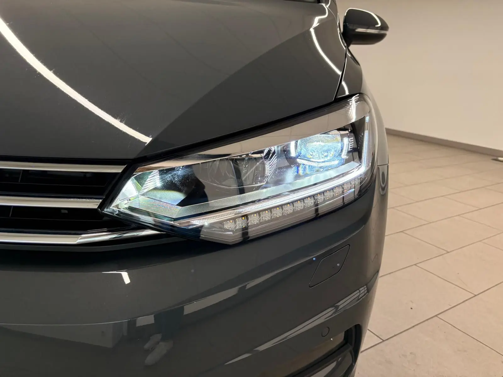 Gros plan sur le phare avant droit du Volkswagen Touran 2025 gris dauphin avec peinture métallisée brillante.