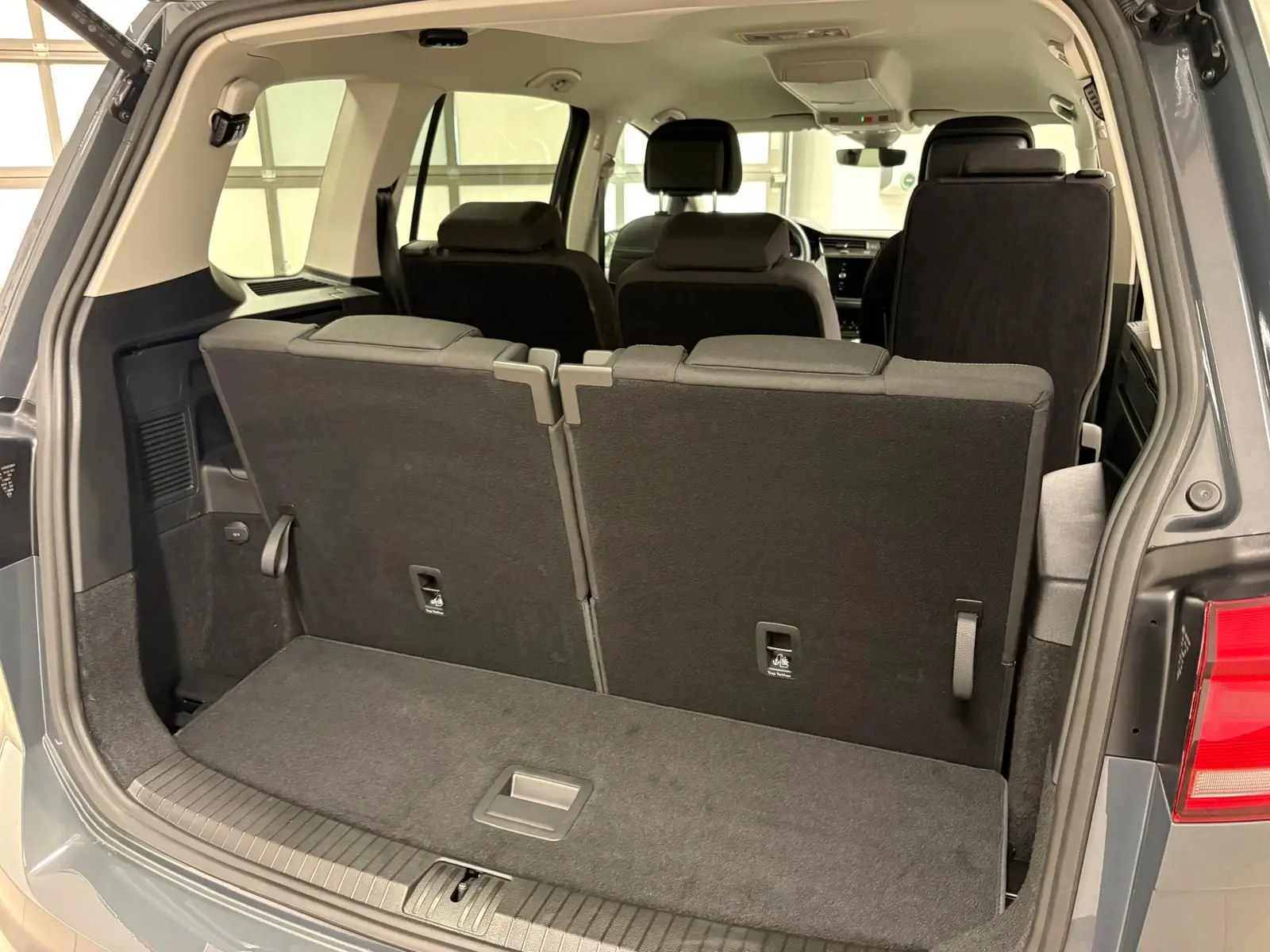 Vue arrière ouverte du coffre du Volkswagen Touran gris dauphin, montrant les sièges arrière relevés et l'intérieur spacieux.