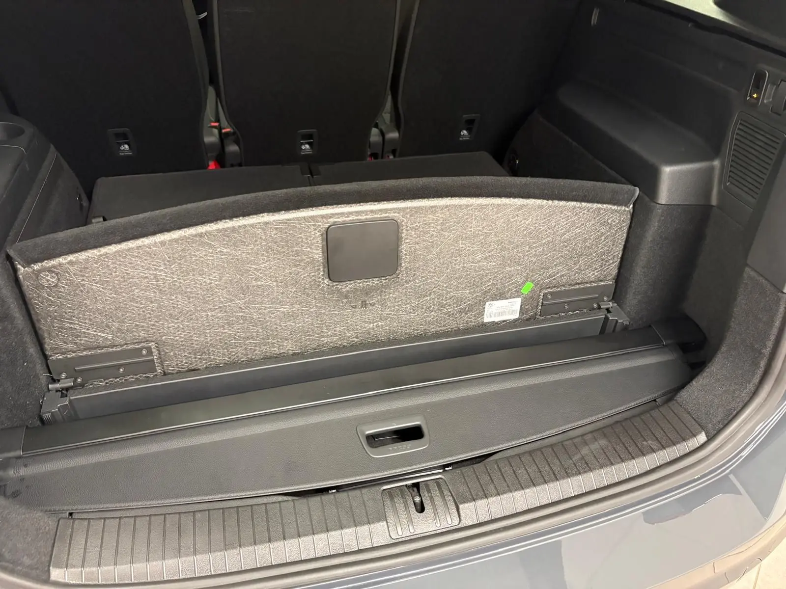 Coffre ouvert du Volkswagen Touran gris dauphin, montrant la banquette arrière et le cache-bagages rétractable.