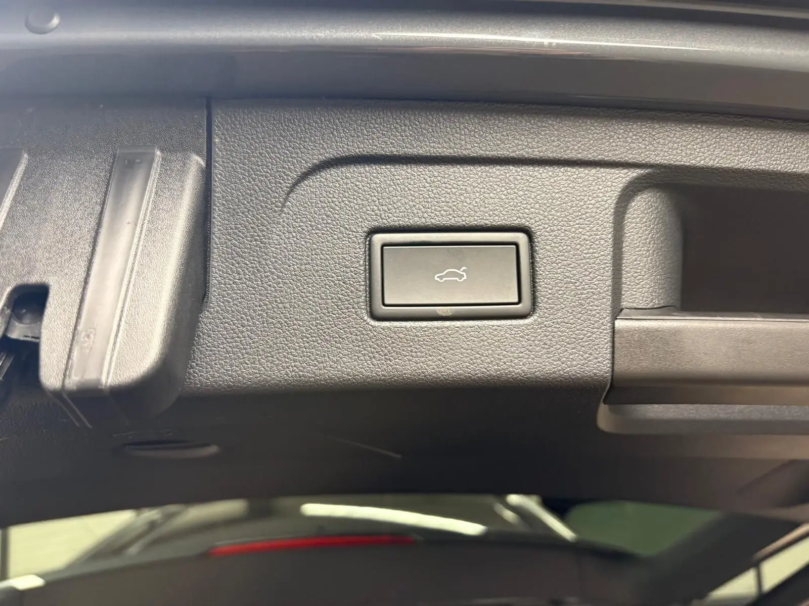 Bouton d'ouverture électrique du hayon sur la partie intérieure du coffre du Volkswagen Touran gris dauphin.