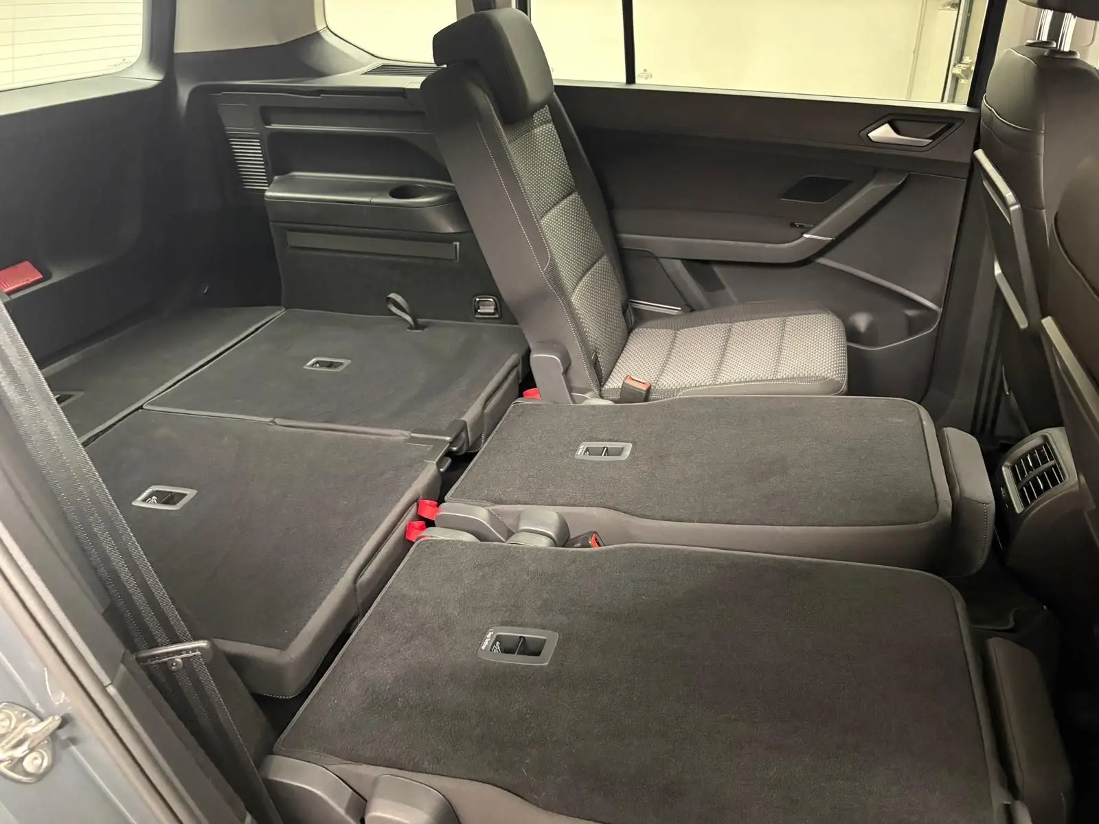 Vue intérieure côté droit du Volkswagen Touran 2025, sièges arrière partiellement rabattus avec sellerie grise.