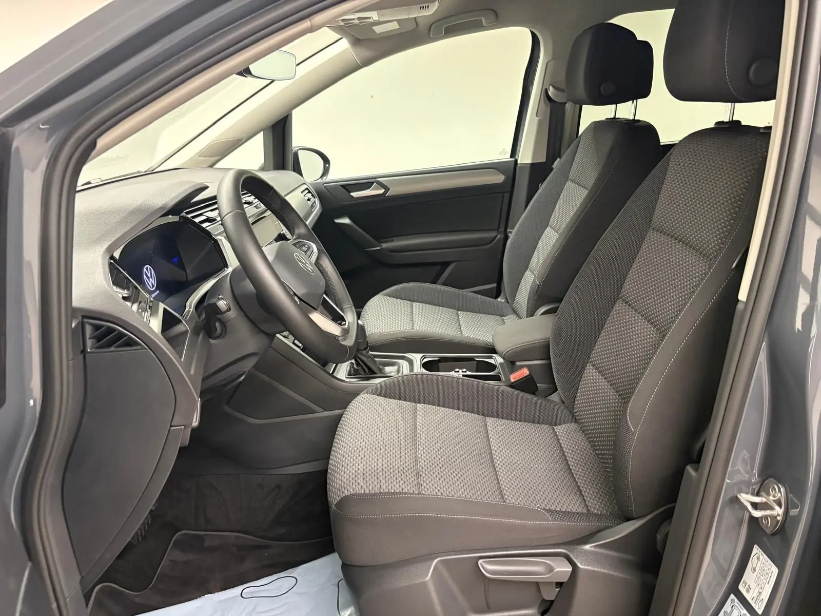 Vue intérieure côté conducteur du Volkswagen Touran gris dauphin, montrant les sièges avant et le tableau de bord moderne.