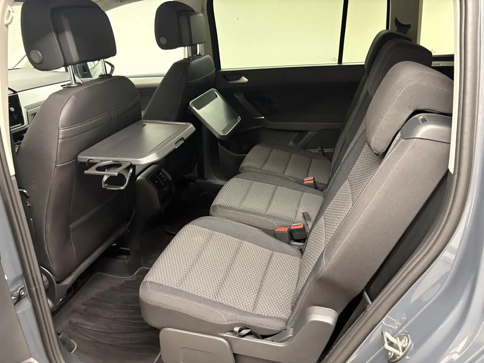Vue latérale droite de l'intérieur arrière du Volkswagen Touran gris Dauphin avec tablette rabattable et sièges tissu gris.