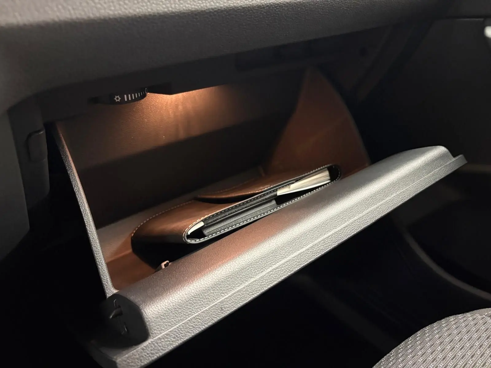 Gant de boîte à gants ouvert avec éclairage intérieur, montrant un carnet noir dans un Volkswagen Touran gris Dauphin.