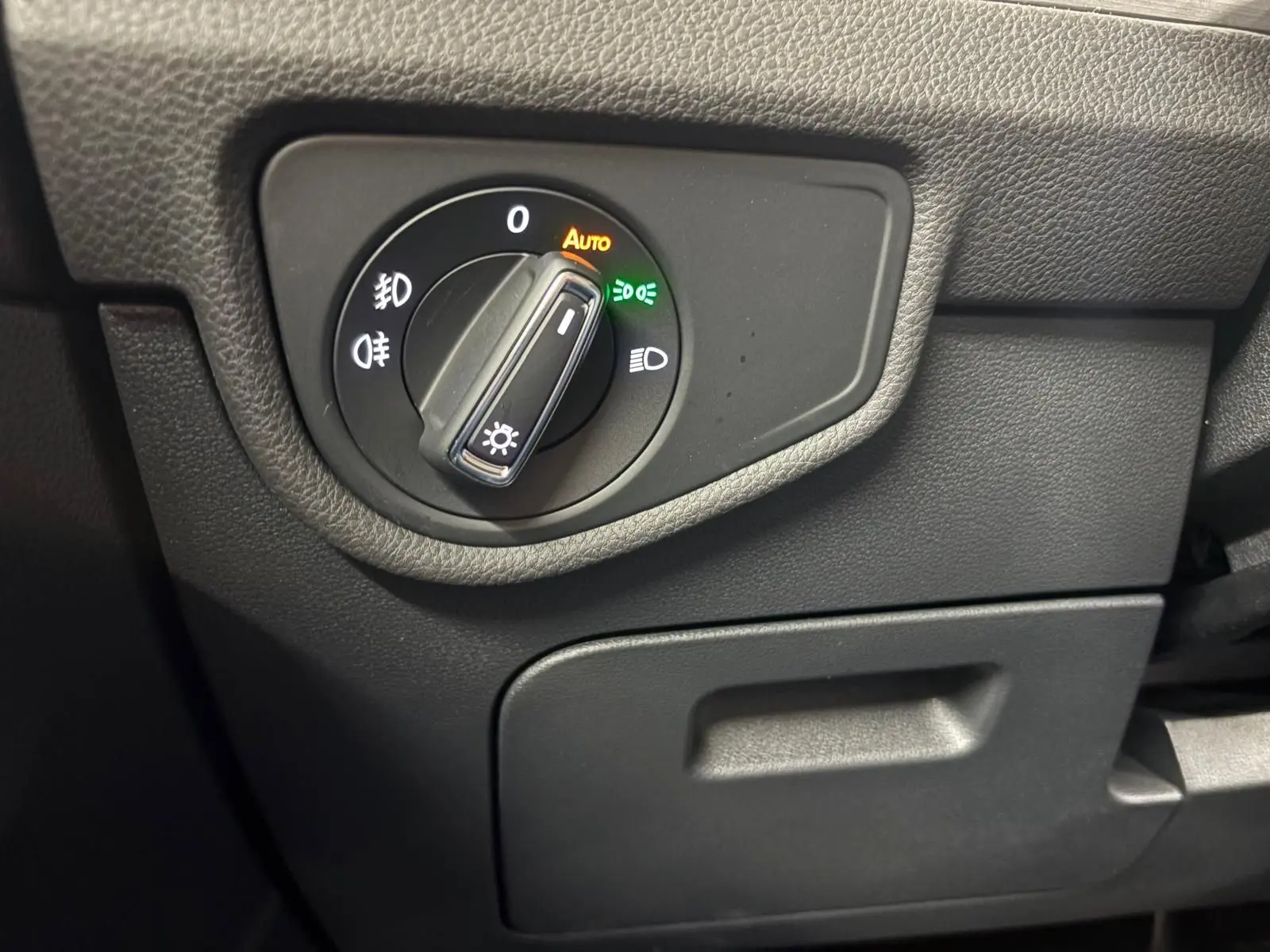 Gros plan sur le bouton de commande des phares du tableau de bord noir du Volkswagen Touran gris Dauphin 2025.