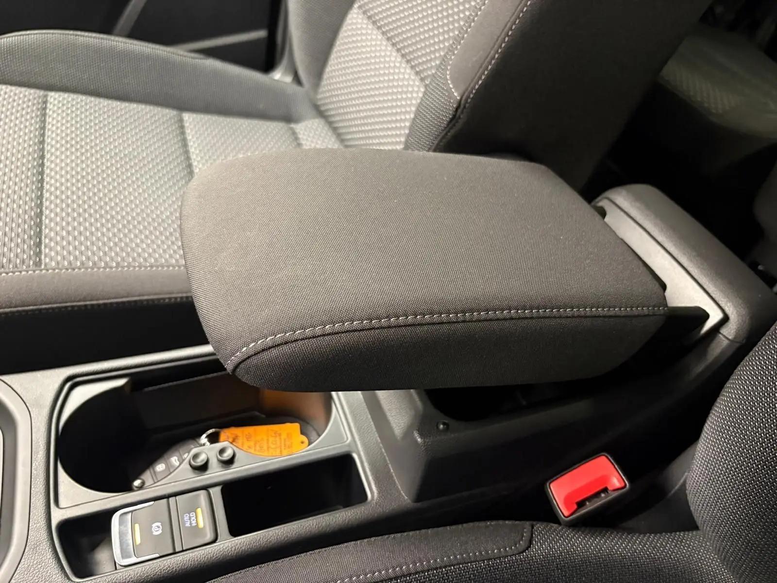 Gros plan sur l'accoudoir central et la console noire intérieure du Volkswagen Touran 2025, tissu gris et détails fonctionnels.