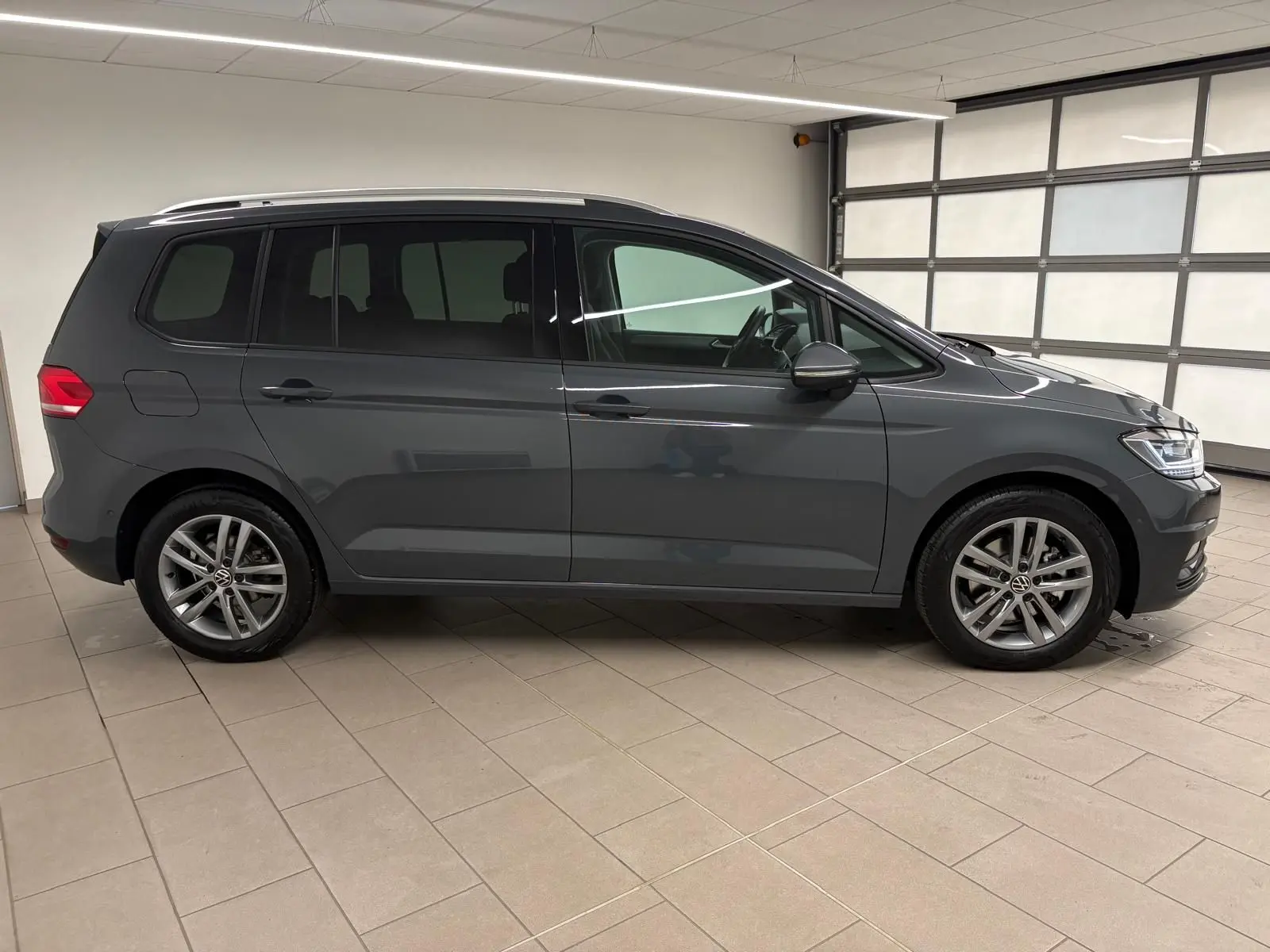 Volkswagen Touran 2.0 TDI gris dauphin vu de profil côté gauche, avec jantes alliage et attelage escamotable.