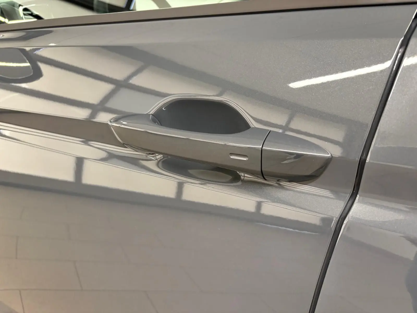 Poignée de porte côté gauche d'un Volkswagen Touran gris dauphin métallisé, vue rapprochée sur la carrosserie lisse.