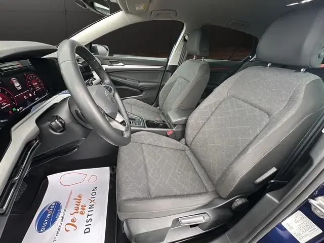 Vue intérieure côté conducteur de la Volkswagen Golf VIII bleu, sièges tissu gris et tableau de bord numérique.