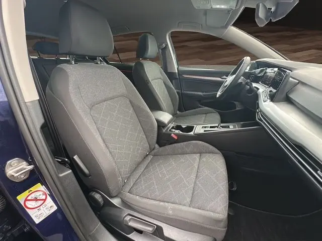 Vue intérieure côté conducteur de la Volkswagen Golf VIII bleu, sièges tissu gris et tableau de bord moderne.