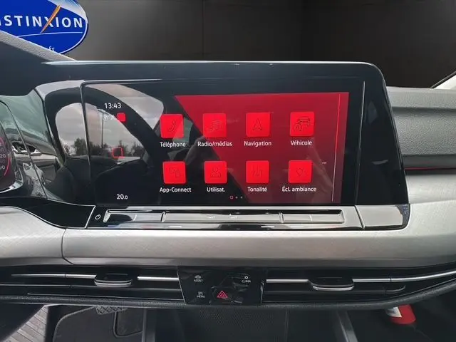 Écran tactile central rouge affichant les menus multimédias dans l'habitacle noir d'une Volkswagen Golf VIII 2023.