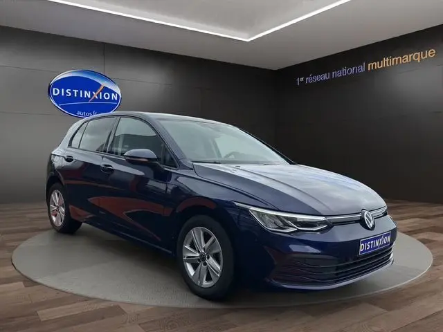 Volkswagen Golf VIII bleu en 3/4 avant droit, avec phares LED et calandre épurée dans un showroom.