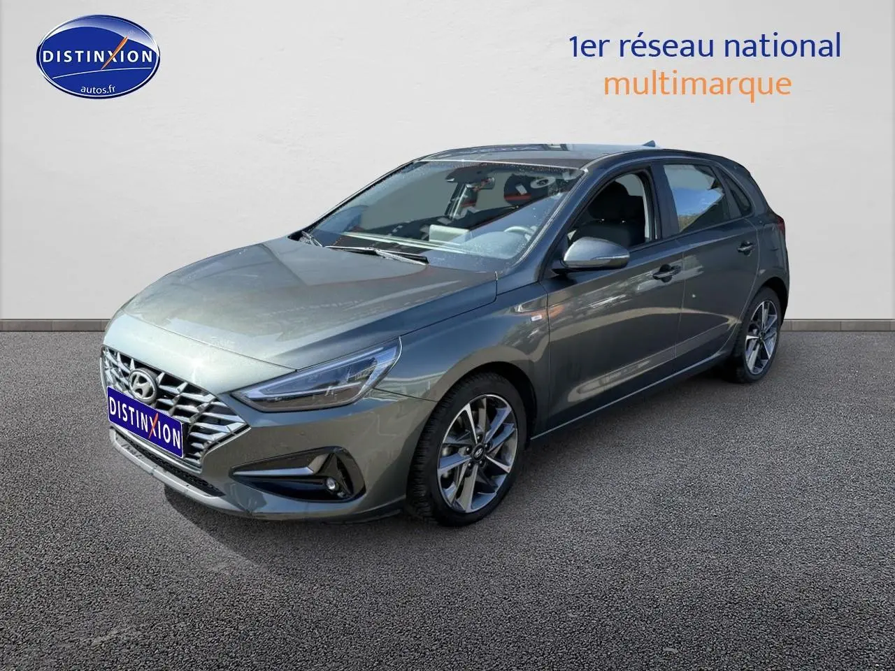 Hyundai i30 gris anthracite vue 3/4 avant droit avec jantes alu et calandre chromée sur fond neutre.