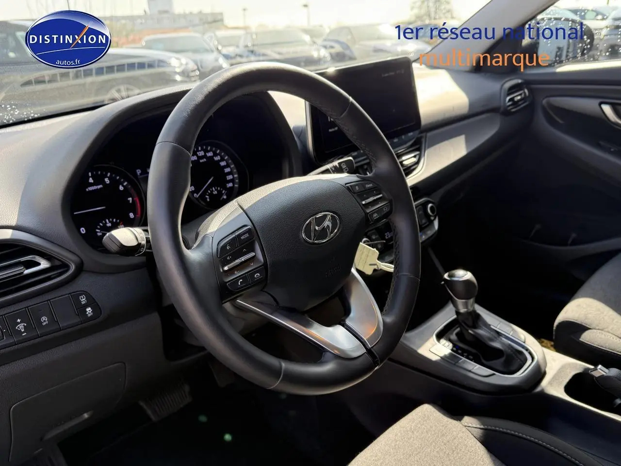 Intérieur de la Hyundai i30 2024 en vue côté conducteur, volant cuir multifonction et console centrale avec boîte auto.