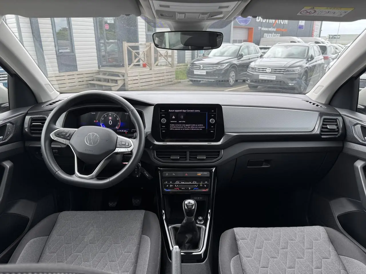 Vue intérieure du tableau de bord et volant du Volkswagen T-Cross 2024 avec écran digital et sellerie grise.
