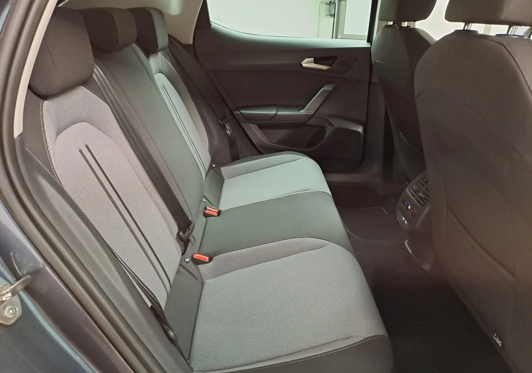Vue intérieure côté gauche des sièges arrière gris clair et foncé du SEAT LEON 1.5 eTSI Hybrid 2025 avec portières ouvertes.