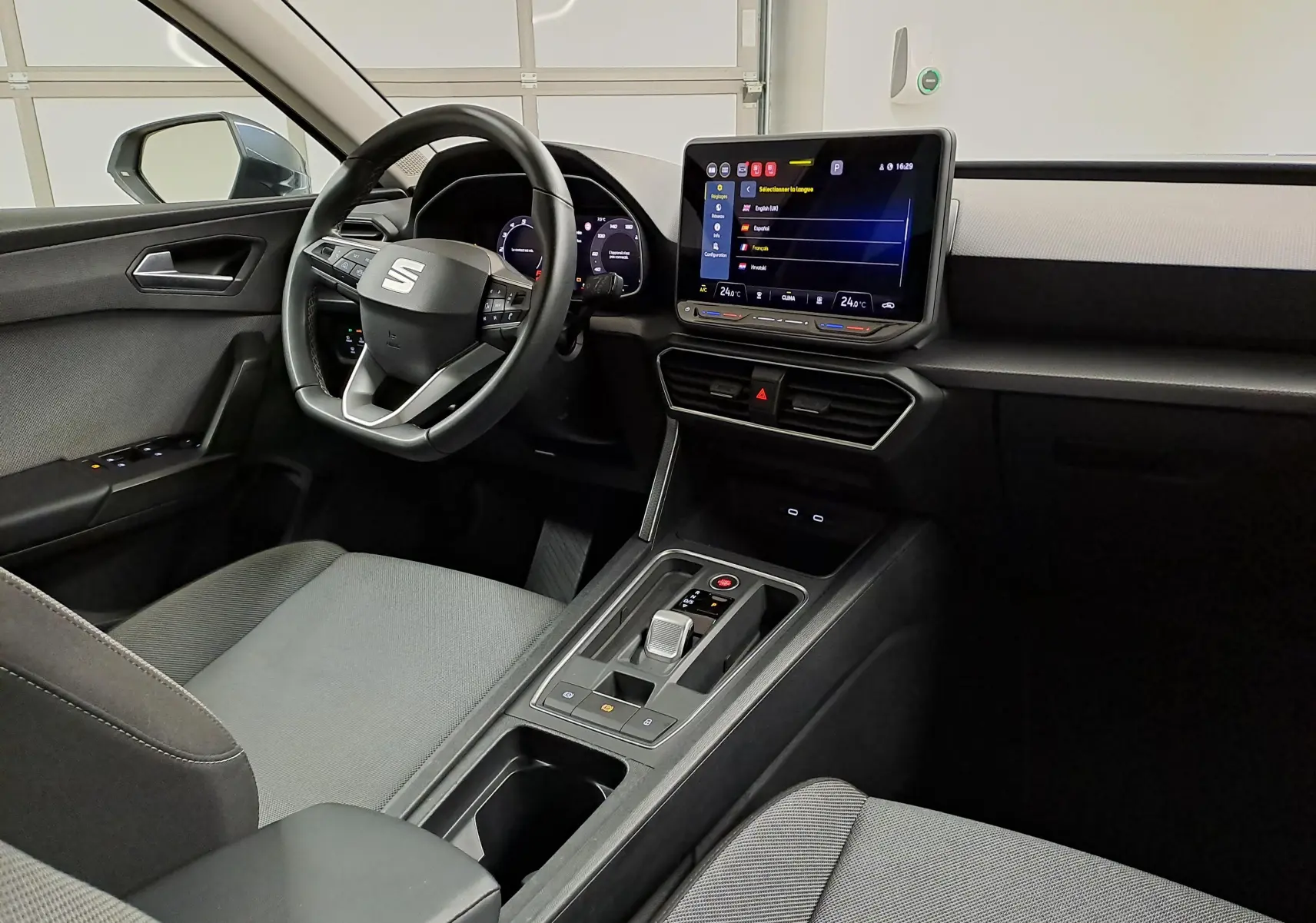 Vue intérieure côté conducteur du SEAT LEON 1.5 eTSI Hybrid 2025, tableau de bord moderne avec écran tactile central.