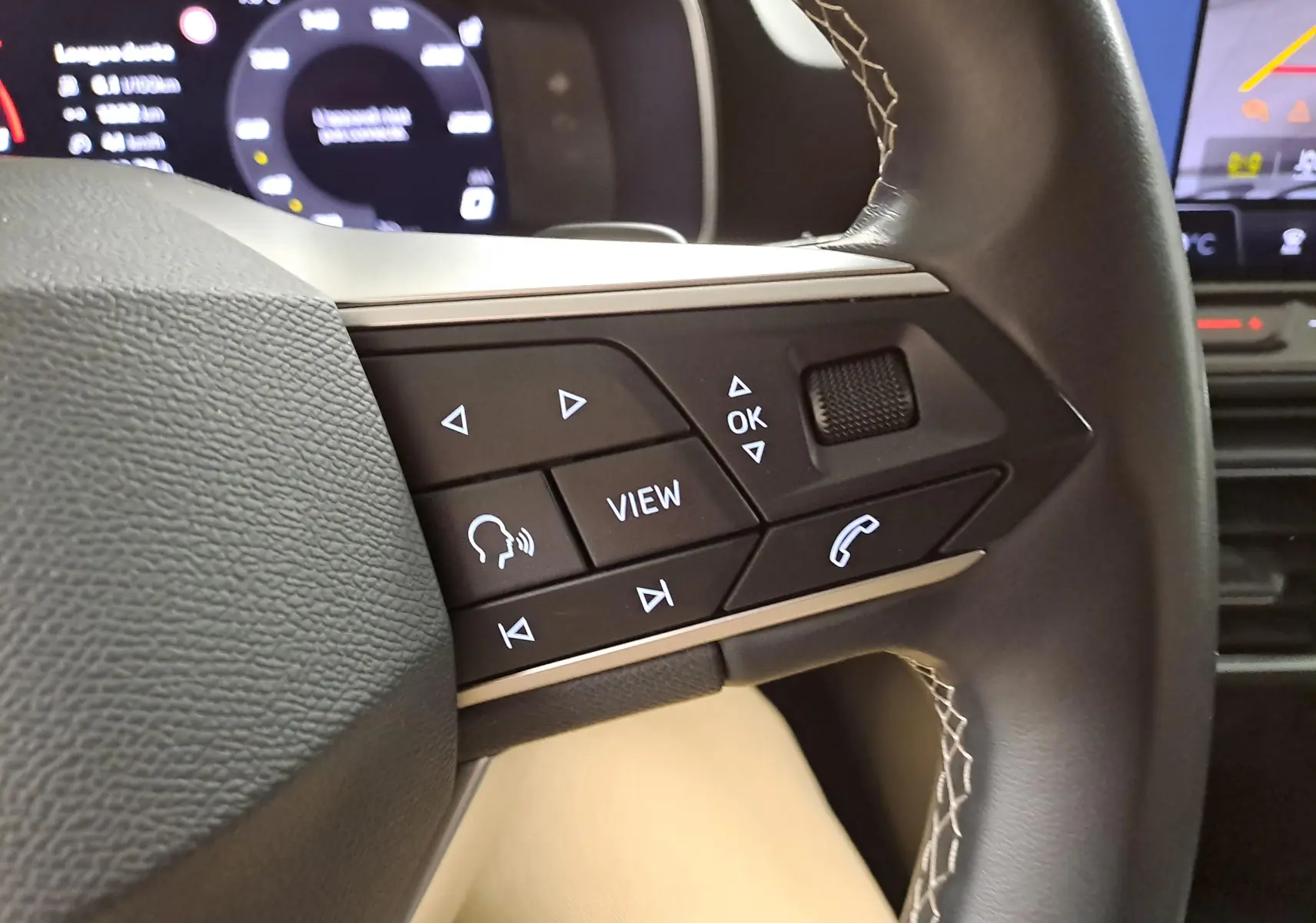 Gros plan sur les commandes au volant du SEAT LEON 1.5 eTSI Hybrid 2025, avec affichage numérique en arrière-plan.