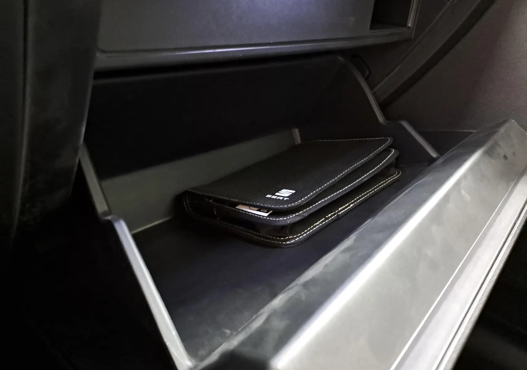 Gros plan sur la boîte à gants ouverte du SEAT LEON 1.5 eTSI Hybrid 2025 avec pochette noire SEAT à l'intérieur.
