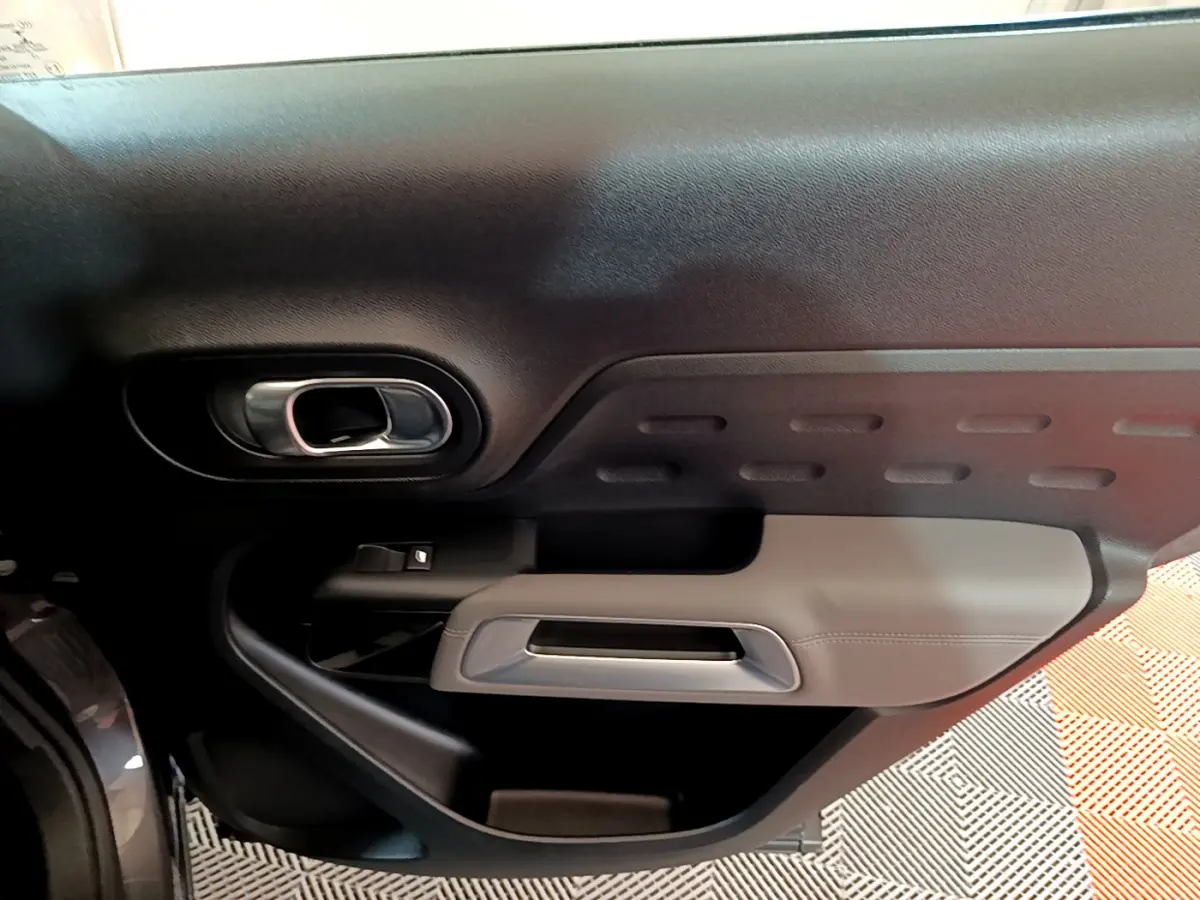 Gros plan sur la porte intérieure côté gauche du Citroën C5 Aircross gris foncé, avec poignée argentée et garniture noire et grise.