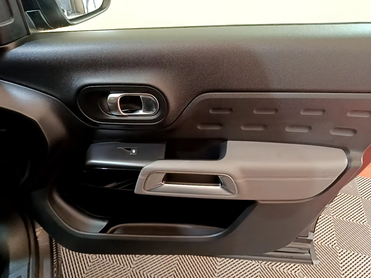 Gros plan sur la porte intérieure côté gauche du Citroën C5 Aircross gris foncé, avec poignée argentée et panneau noir texturé.