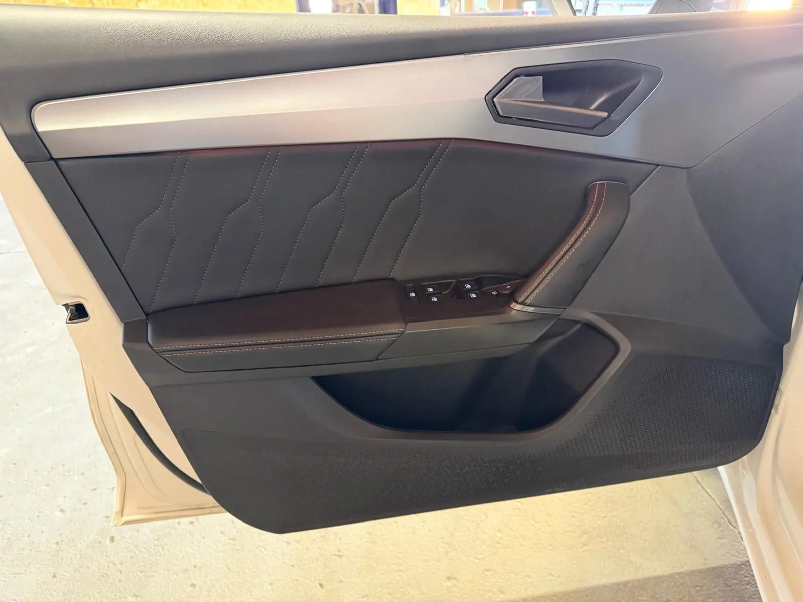 Vue rapprochée de la porte avant gauche noire avec surpiqûres et commandes des vitres d'une CUPRA LEON ST blanche 2024.