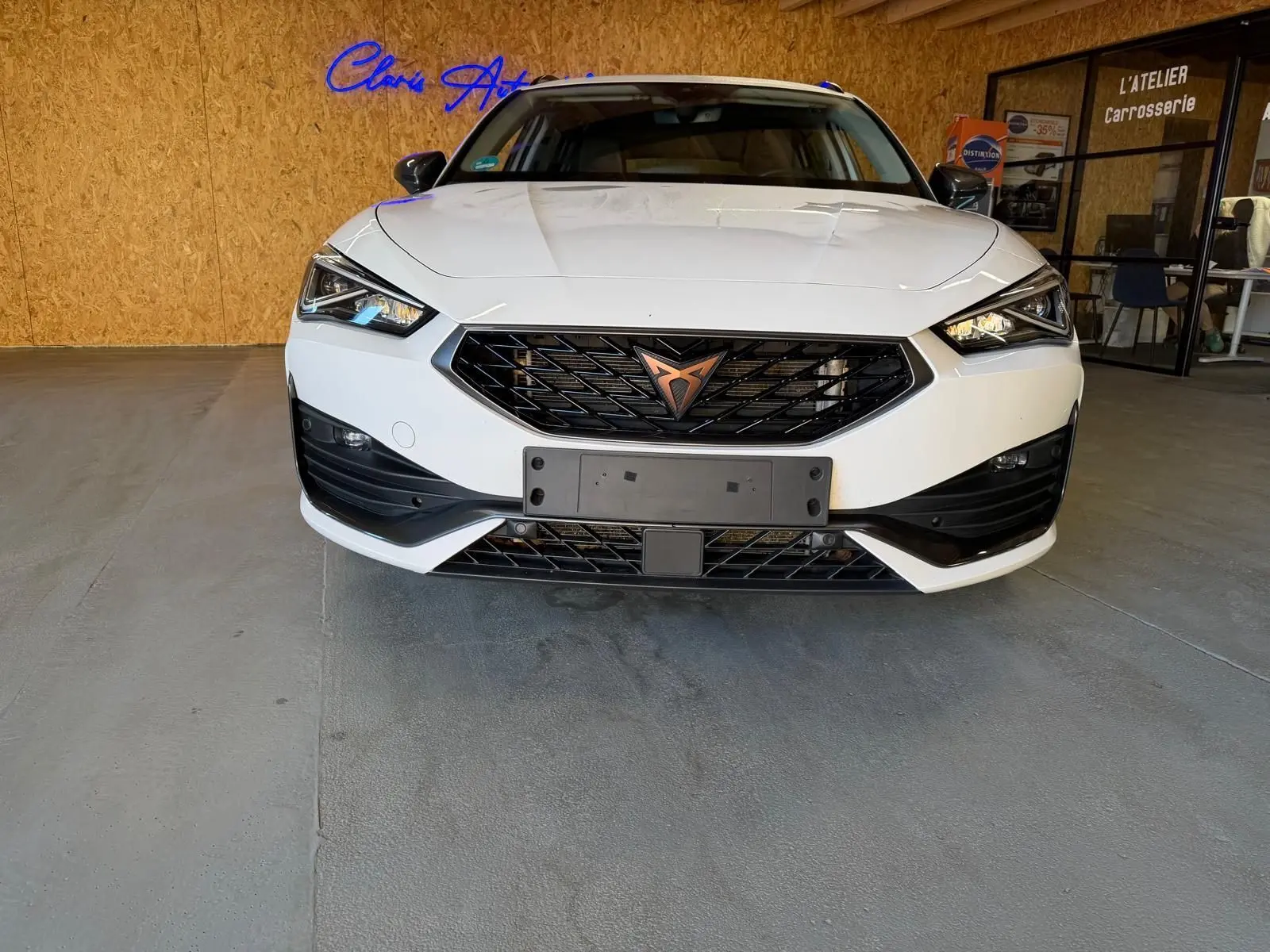 Vue frontale d'une CUPRA LEON ST blanche 2024 avec calandre noire et logo cuivre, dans un garage intérieur.