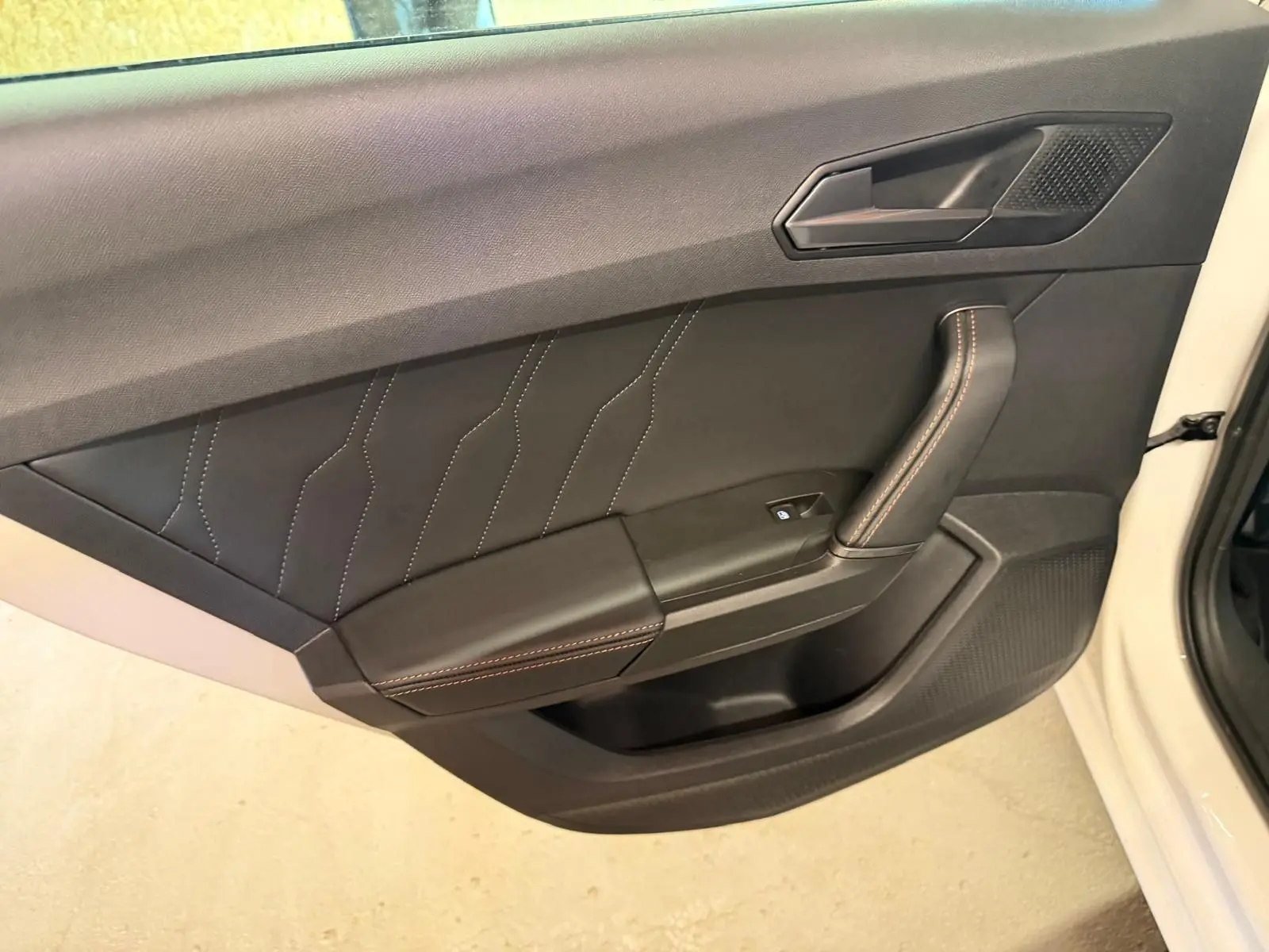 Vue intérieure côté gauche de la porte avant blanche d'une CUPRA LEON ST 2024 avec garniture noire et surpiqûres contrastantes.