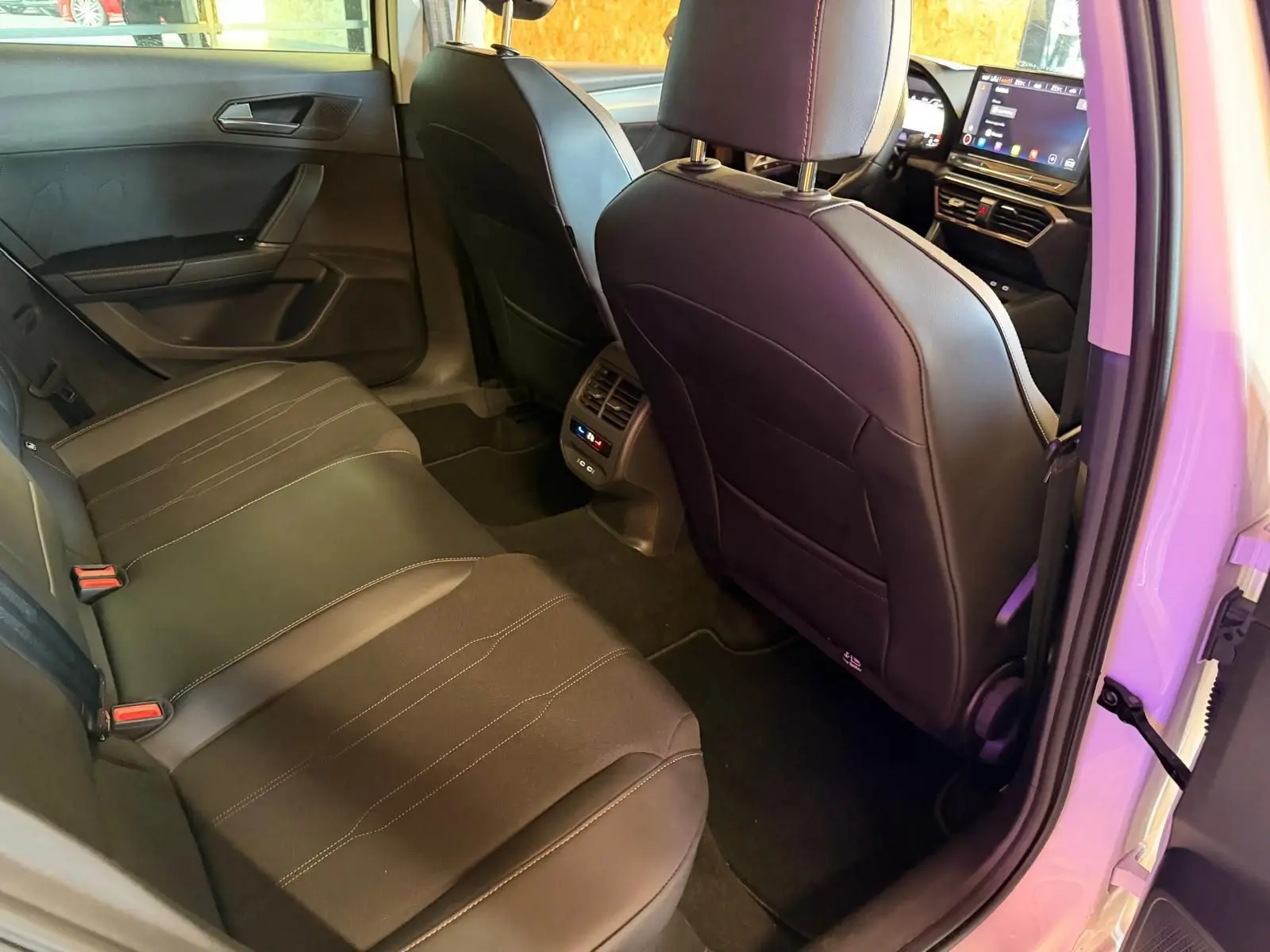 Vue intérieure arrière droite de la CUPRA LEON ST 2024 blanche, montrant les sièges noirs et la console centrale avec commandes climatisation.