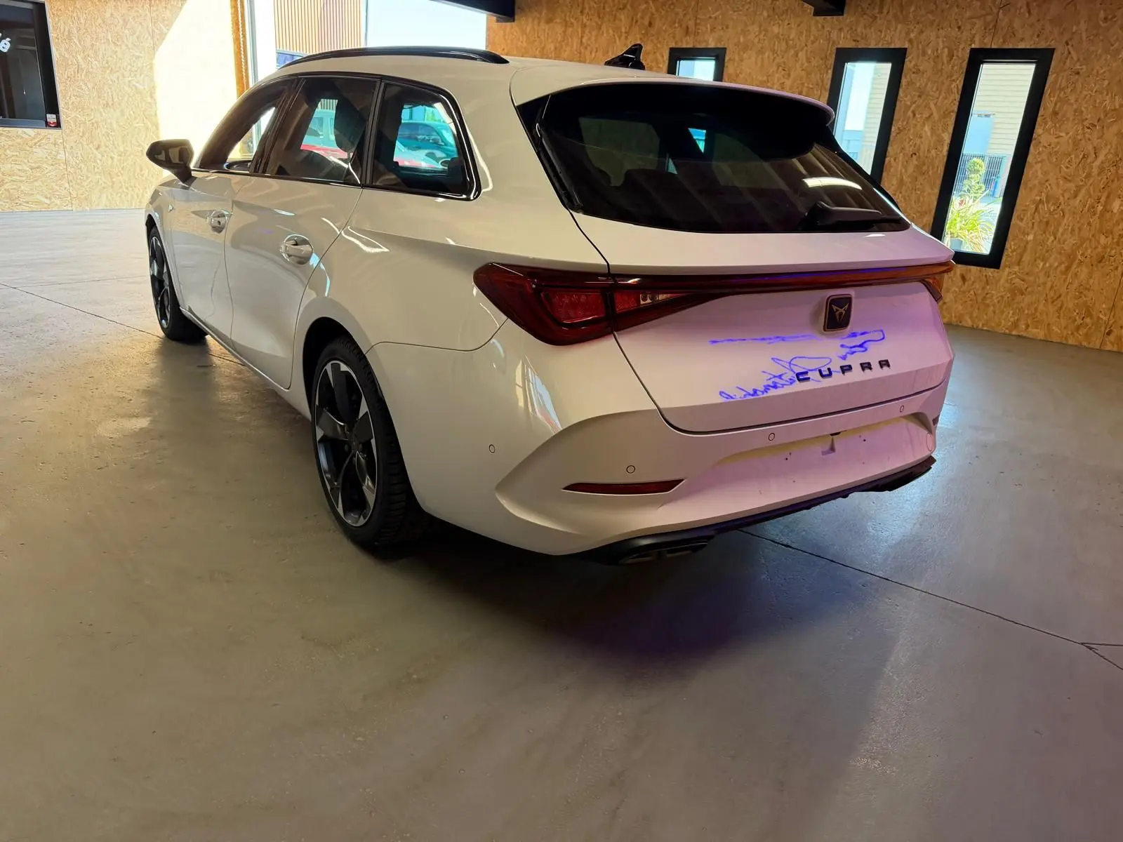 Vue 3/4 arrière droite d'une CUPRA LEON ST blanche 2024 avec feux arrière reliés et jantes noires distinctives.