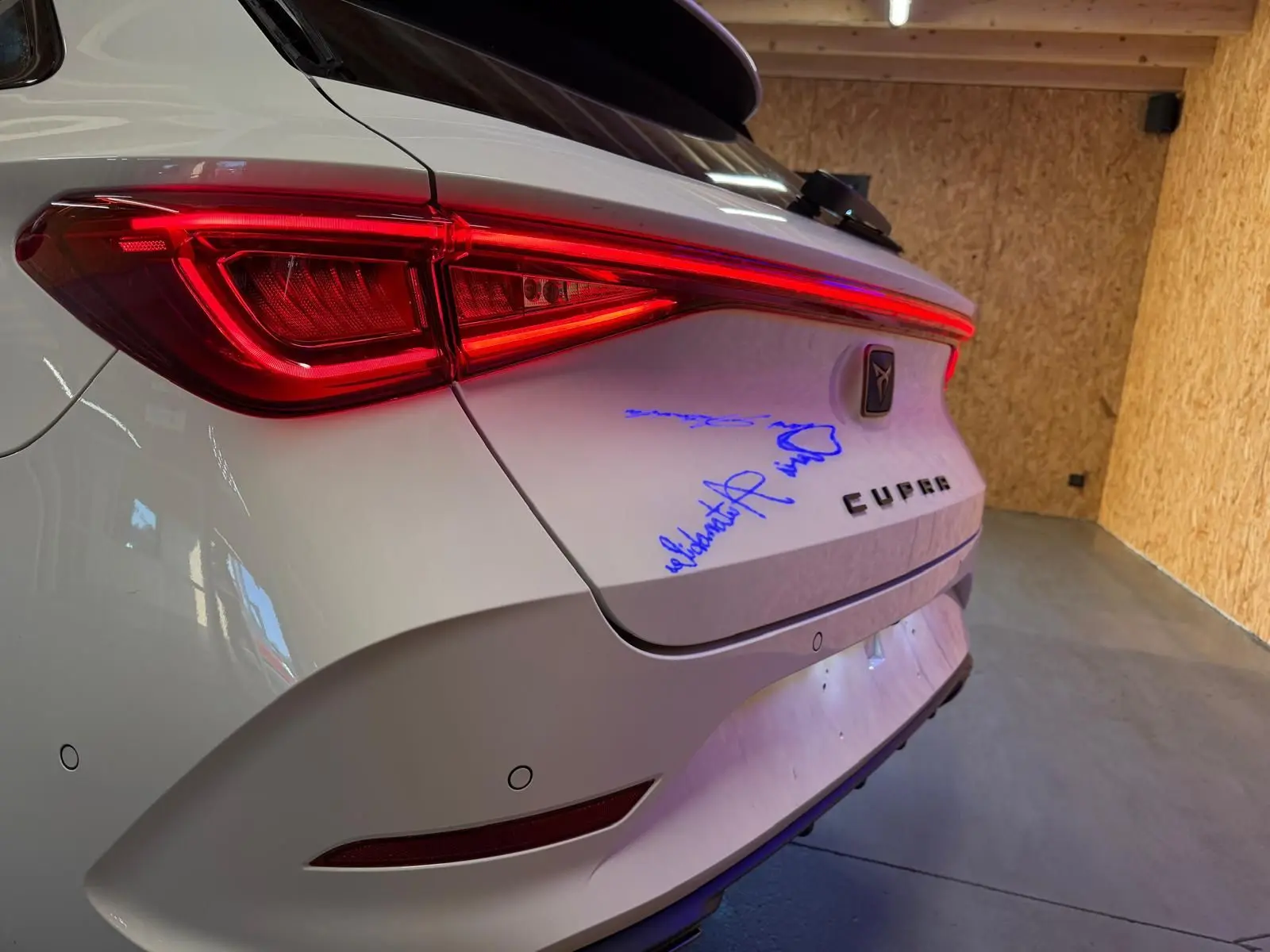 Vue arrière droite d'une CUPRA LEON ST blanche 2024 avec feux LED allumés et signature bleue sur le coffre.