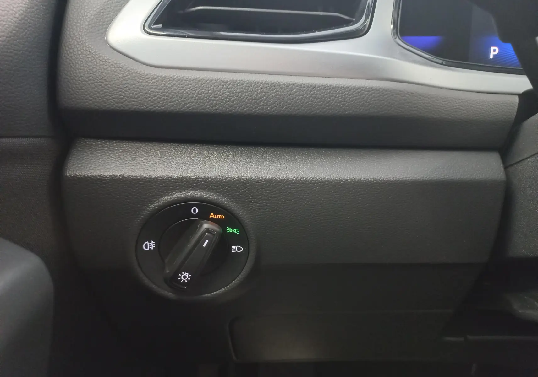 Détail intérieur du Volkswagen T-Roc 2025 gris Indium montrant la commande des phares côté gauche du tableau de bord.