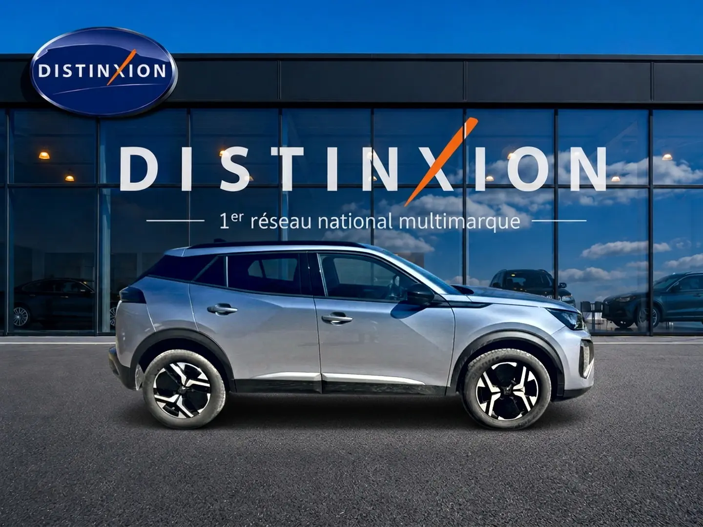 Peugeot 2008 1.2 100 Allure gris Artense vue de profil côté gauche devant une vitrine avec logo Distinxion.