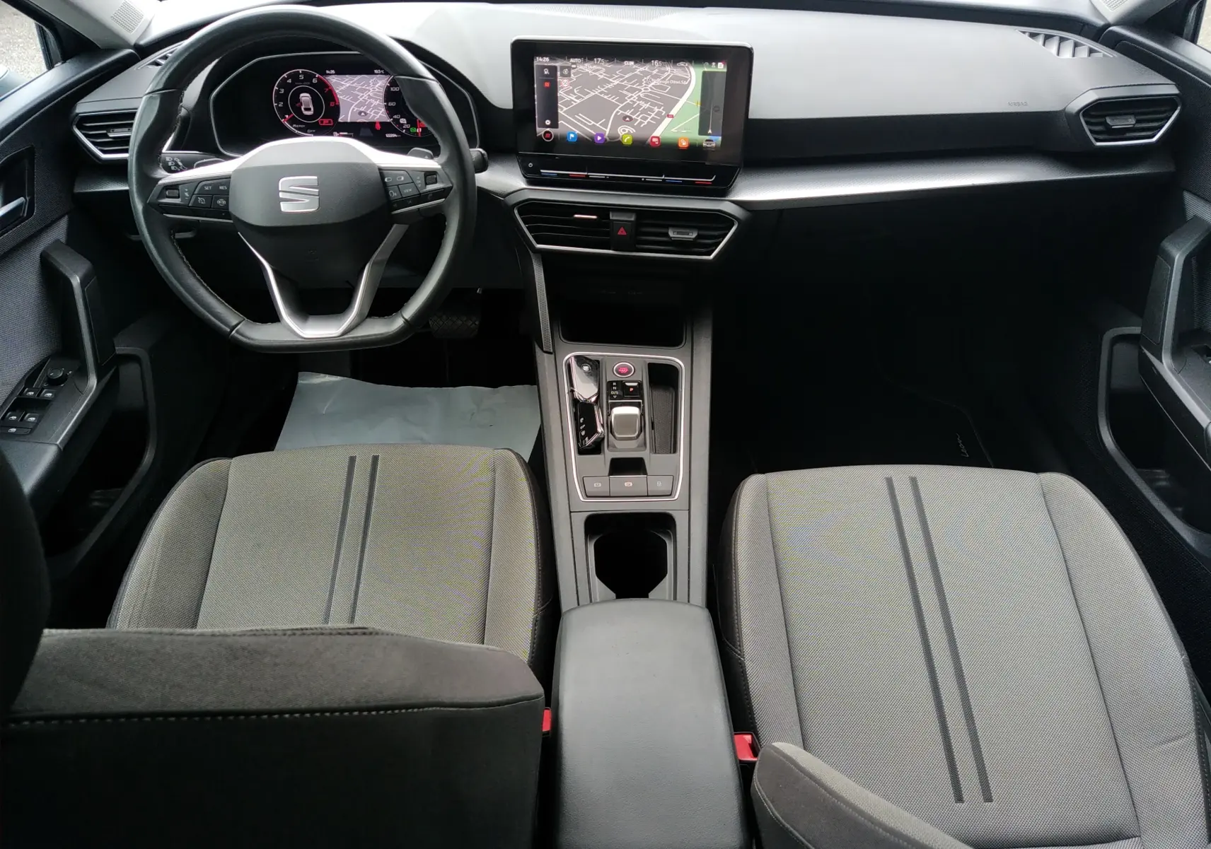 Vue intérieure avant de la SEAT LEON ST grise, montrant le volant multifonction, l’écran tactile GPS et les sièges tissu gris.