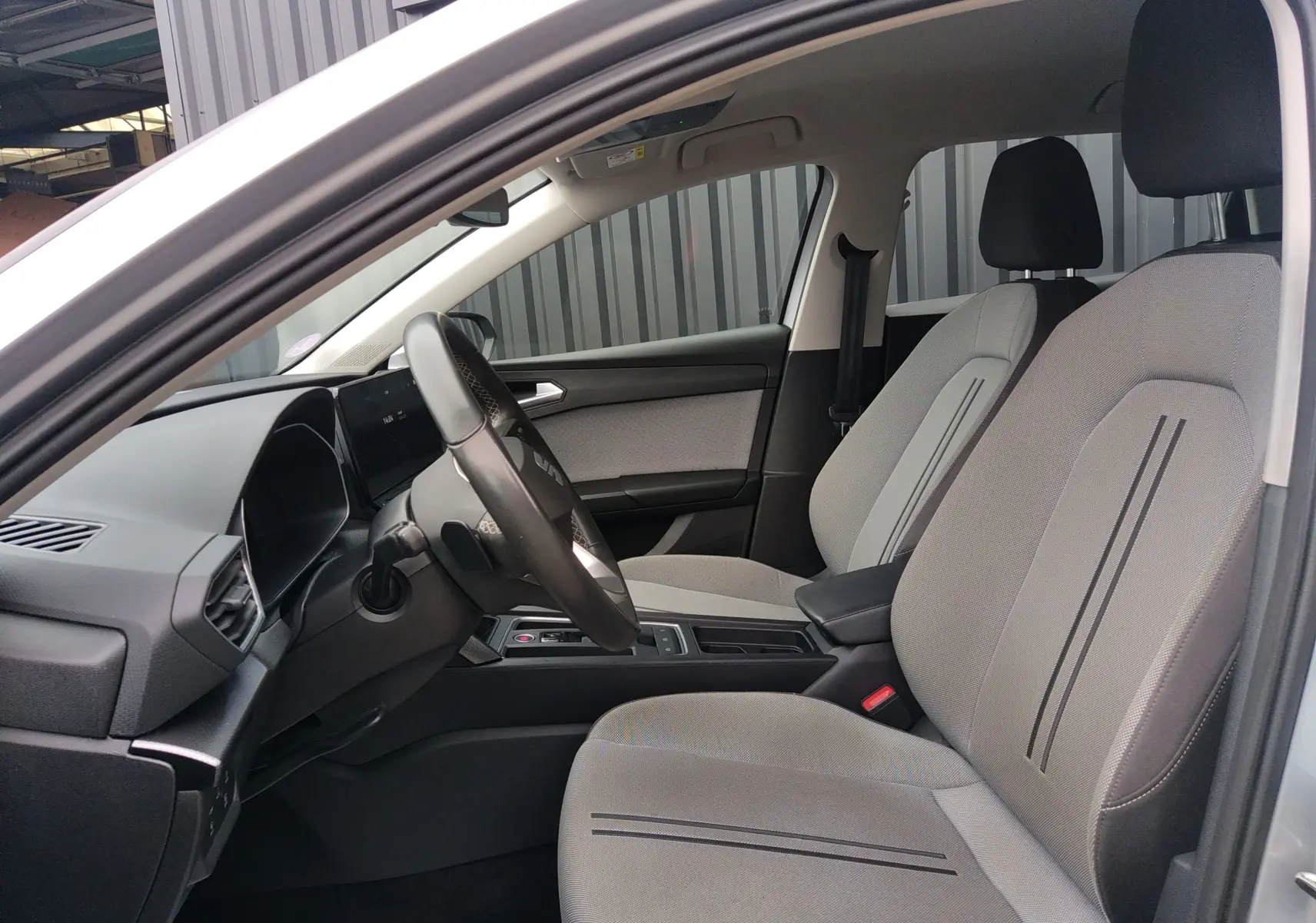 Vue intérieure côté conducteur de la SEAT LEON ST gris 2022, mettant en valeur les sièges tissu gris et le tableau de bord moderne.