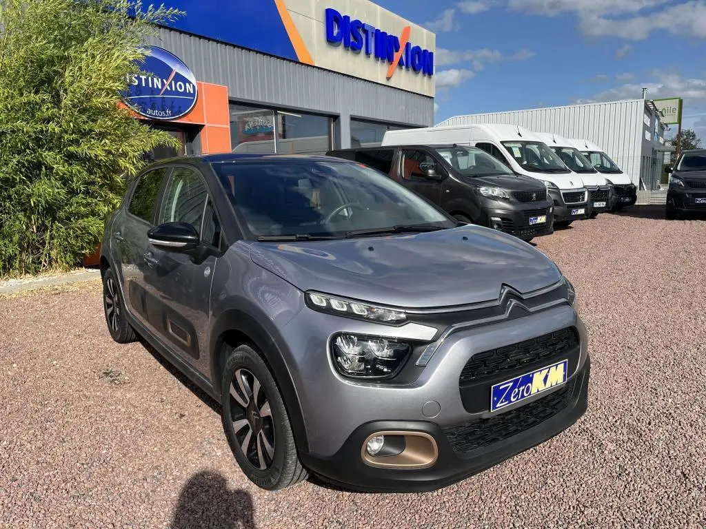 Citroën C3 gris en 3/4 avant droit, avec projecteurs LED et détails noirs contrastants sur carrosserie nacrée.