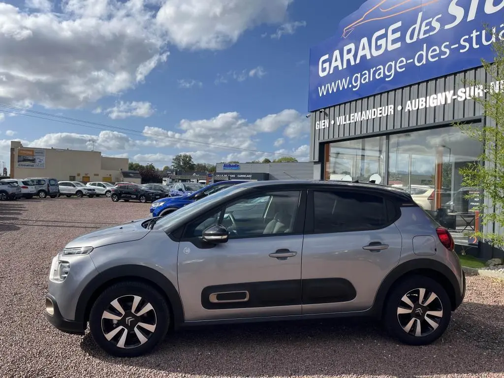 Profil droit d'une Citroën C3 gris nacré 2022 avec toit noir et protections latérales noires sur un parking extérieur.