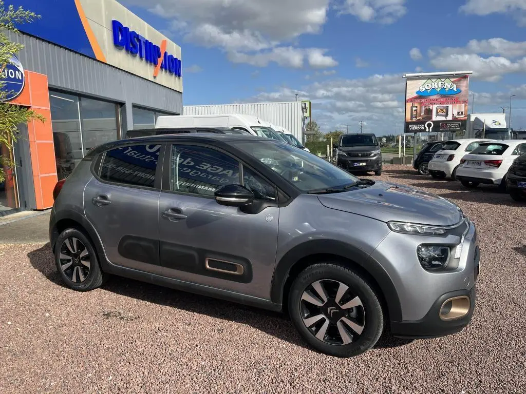 Vue de profil côté gauche d'une Citroën C3 gris métallisé avec toit noir et protections latérales distinctives.
