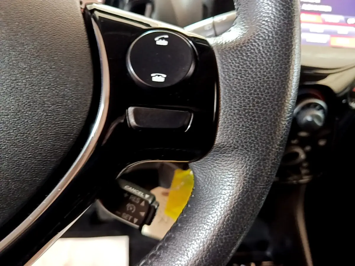 Gros plan sur le volant cuir noir de la Citroën C1 2019 avec commandes intégrées et tableau de bord flou en arrière-plan.