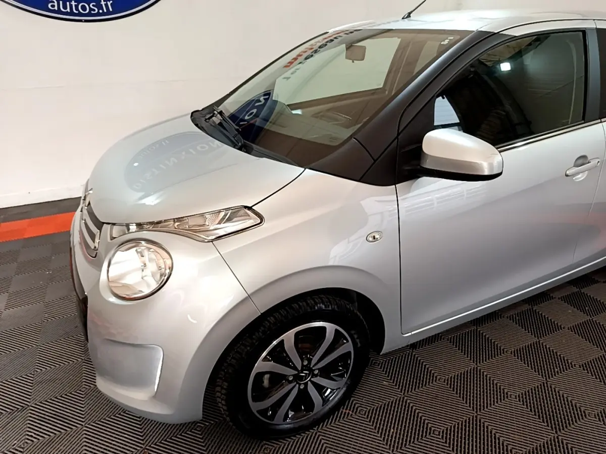 Vue 3/4 avant droit d'une Citroën C1 gris clair avec jantes alliage et rétroviseurs assortis.