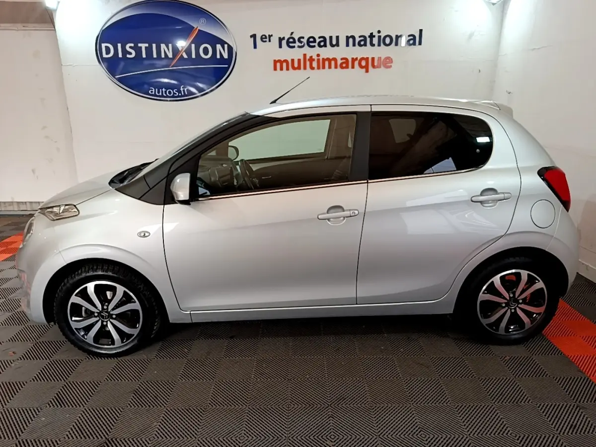 Profil droit d'une Citroën C1 gris clair 2019 avec jantes noires et argentées, dans un showroom intérieur.