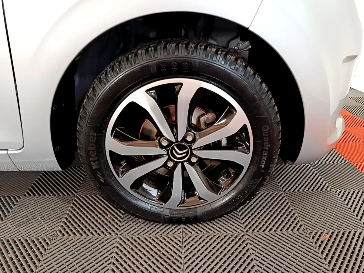 Gros plan sur la roue avant droite d'une Citroën C1 gris clair, mettant en valeur la jante alliage bicolore.