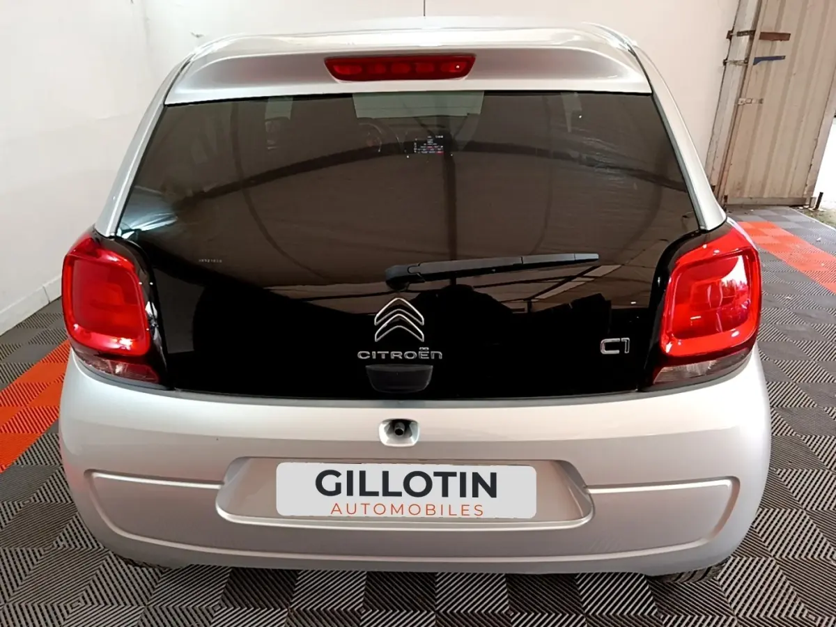 Vue arrière d’une Citroën C1 gris clair avec hayon noir et feux arrière rouges dans un garage.