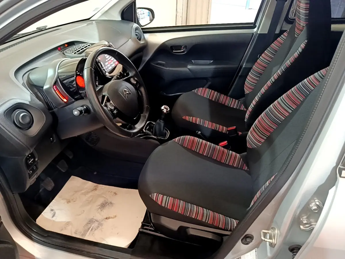 Intérieur avant droit de la Citroën C1 gris clair 2019, sièges tissu rayé, volant cuir multifonctions et boîte manuelle.